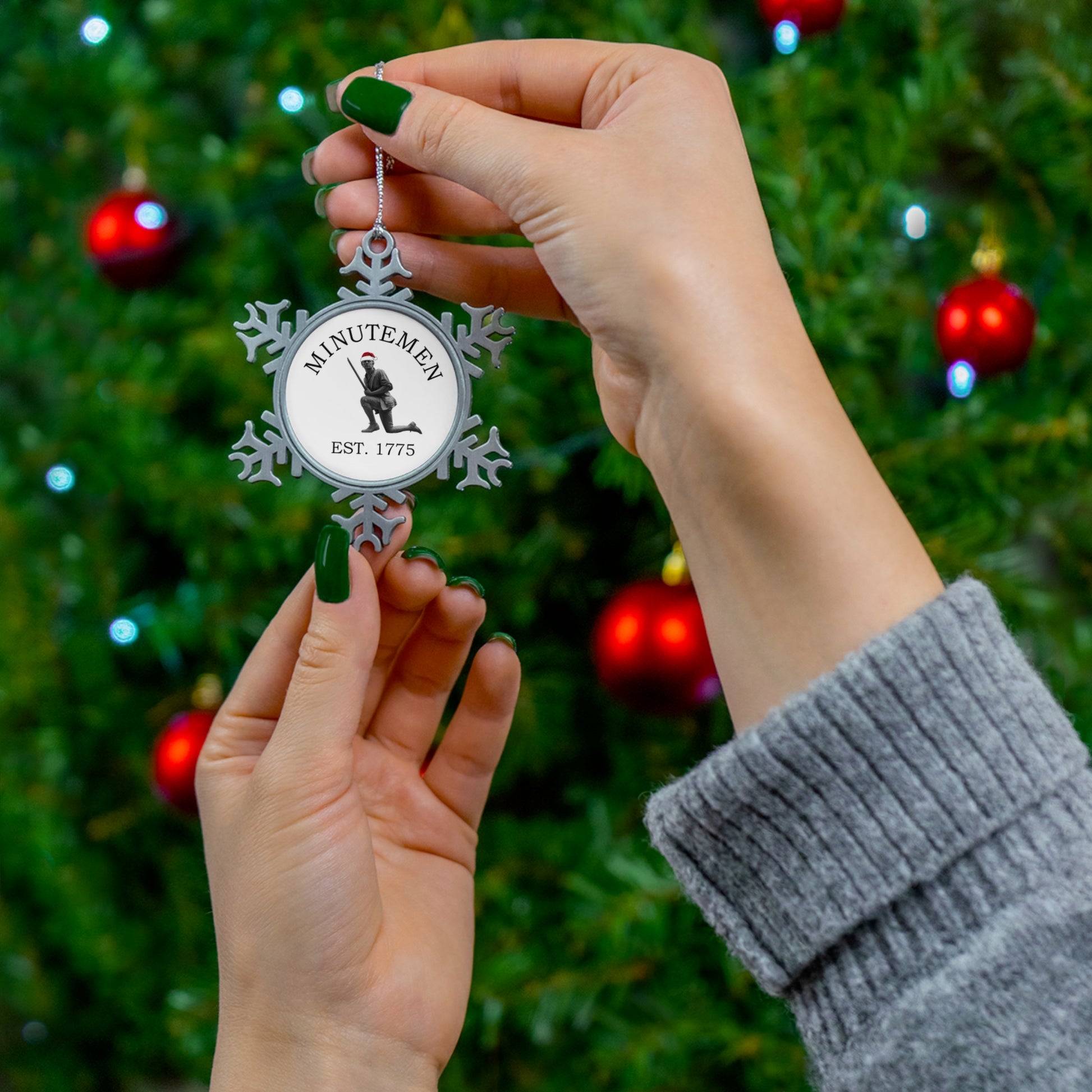 Minuteman pewter snowflake ornament held before a Christmas tree — silver snowflake ornament with printed center
