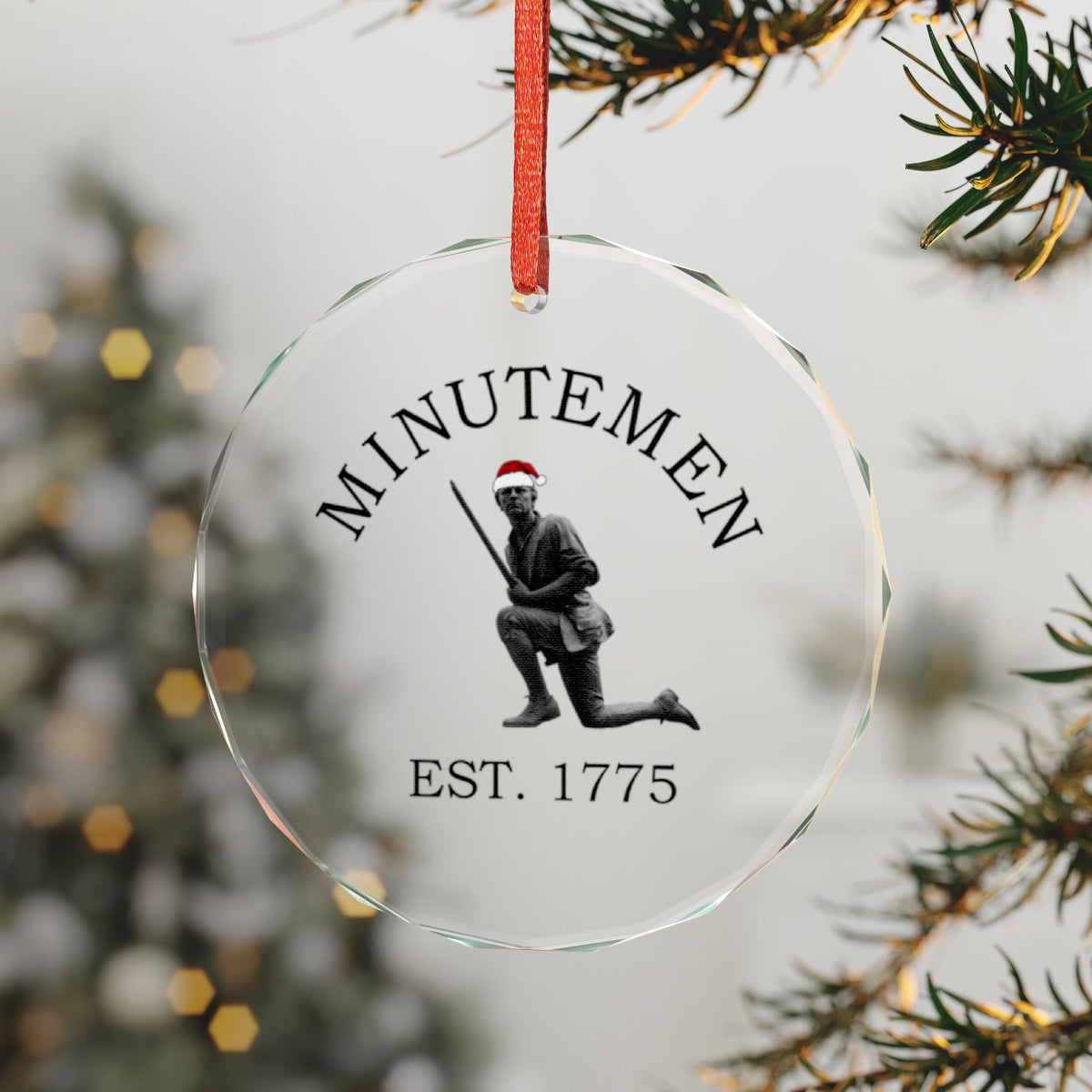 Minuteman crystal glass ornament hanging by a red ribbon — kneeling minute man with Santa hat, faceted beveled edge