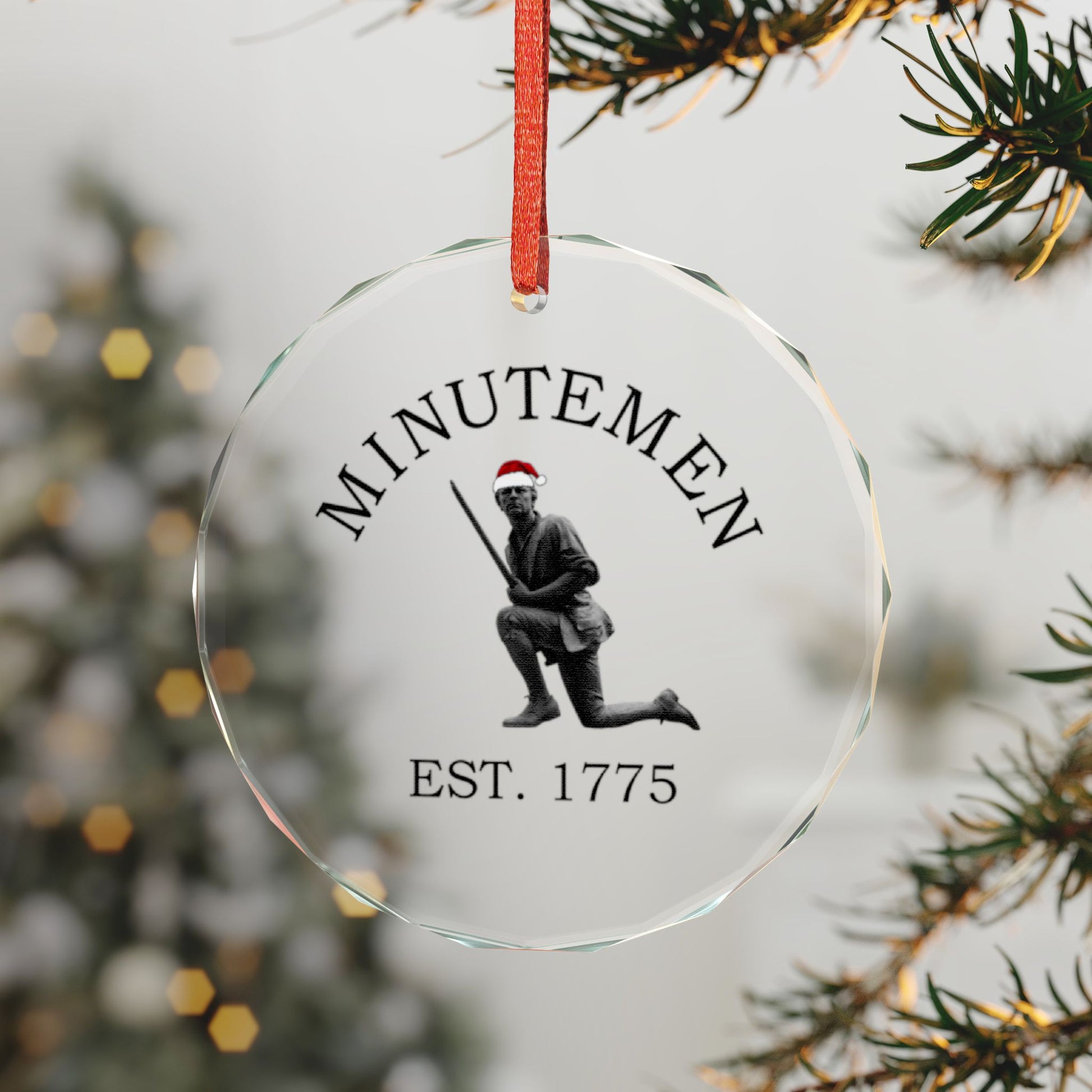Minuteman crystal glass ornament hanging by a red ribbon — kneeling minute man with Santa hat, faceted beveled edge